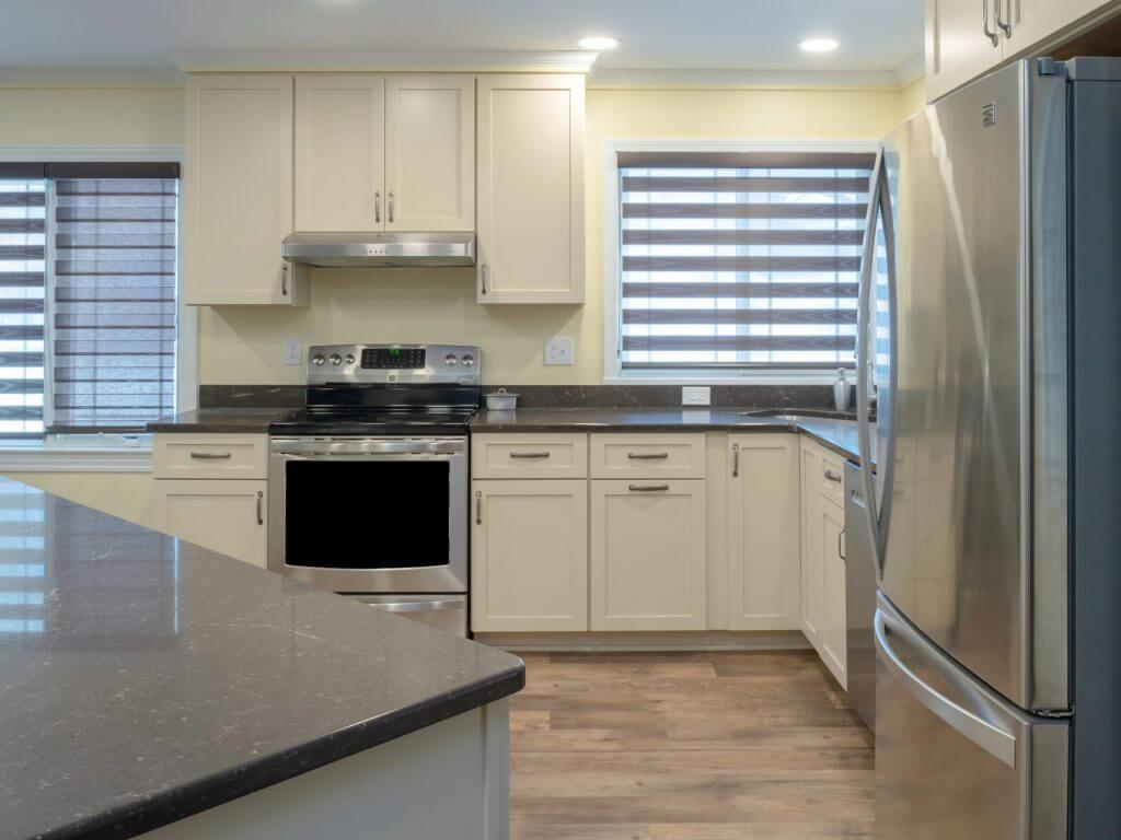updated kitchen remodel featuring white cabinets, stainless steel range and refrigerator, and dark quartz counters by Odd Fellows Contracting in Lansing, MI