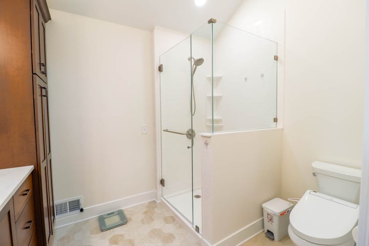 Remodeled primary bathroom in East Lansing MI with a glass corner shower and tile flooring by Odd Fellows Contracting