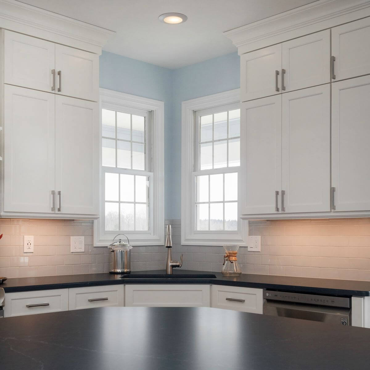 Corner kitchen sink area with white cabinets and subway tile backsplash in Bath Township remodel by Odd Fellows Contracting