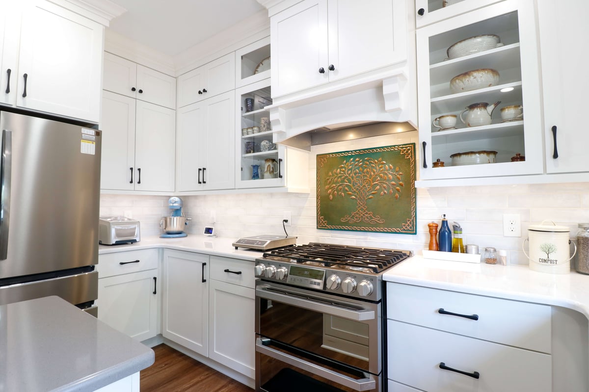 vent hood and gas range, white kitchen cabinets with under cabinet lighting and tile backsplash