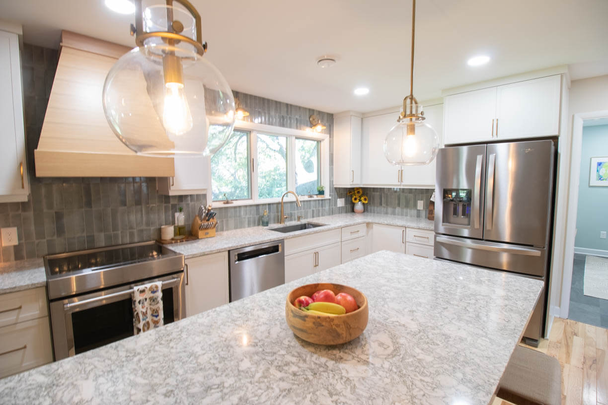 Completed kitchen remodel by Odd Fellows Contracting in Hiawatha Lakes, Okemos, MI showcasing large quartz island and custom wood range hood