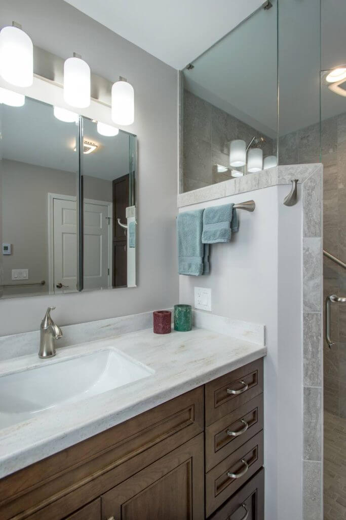 Vanity with quartz countertop beside glass shower enclosure installed by Odd Fellows Contracting in Holt, MI
